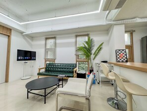 Un espace d’attente moderne comprenant un canapé, une table ronde, un coin bar et un téléviseur fixé au mur.