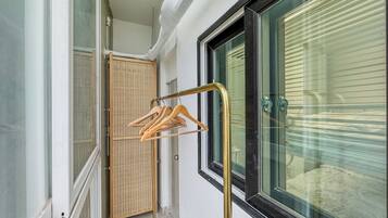 Um corredor estreito com porta de vidro que dá para um quarto, uma porta de madeira e uma janela com persianas.