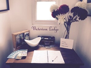 Ein Schreibtisch mit Notizbuch, Stift, einem gerahmten Bild, einer Schale, einer Vase mit Blumen und einem Schild mit WLAN-Informationen und Passwort.