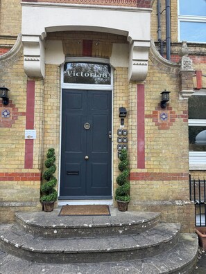 A Victorian Lodge entrance with a dark blue door, two potted topiary plants, a small set of stone steps, and a traditional brick facade. - The Victorian Lodge (Ryde)