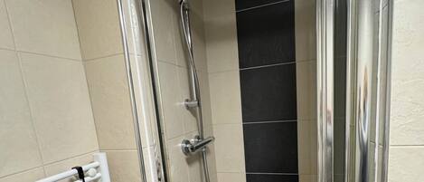 Una ducha con cerramiento de vidrio, pared con azulejos blancos y una sección con azulejos negros.