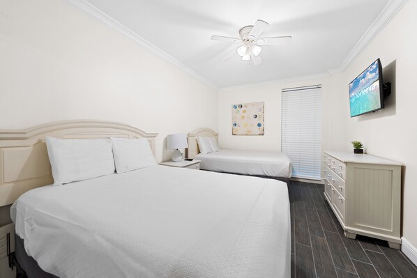 A hotel room with two beds, a ceiling fan, a TV, a painting, and a dresser.