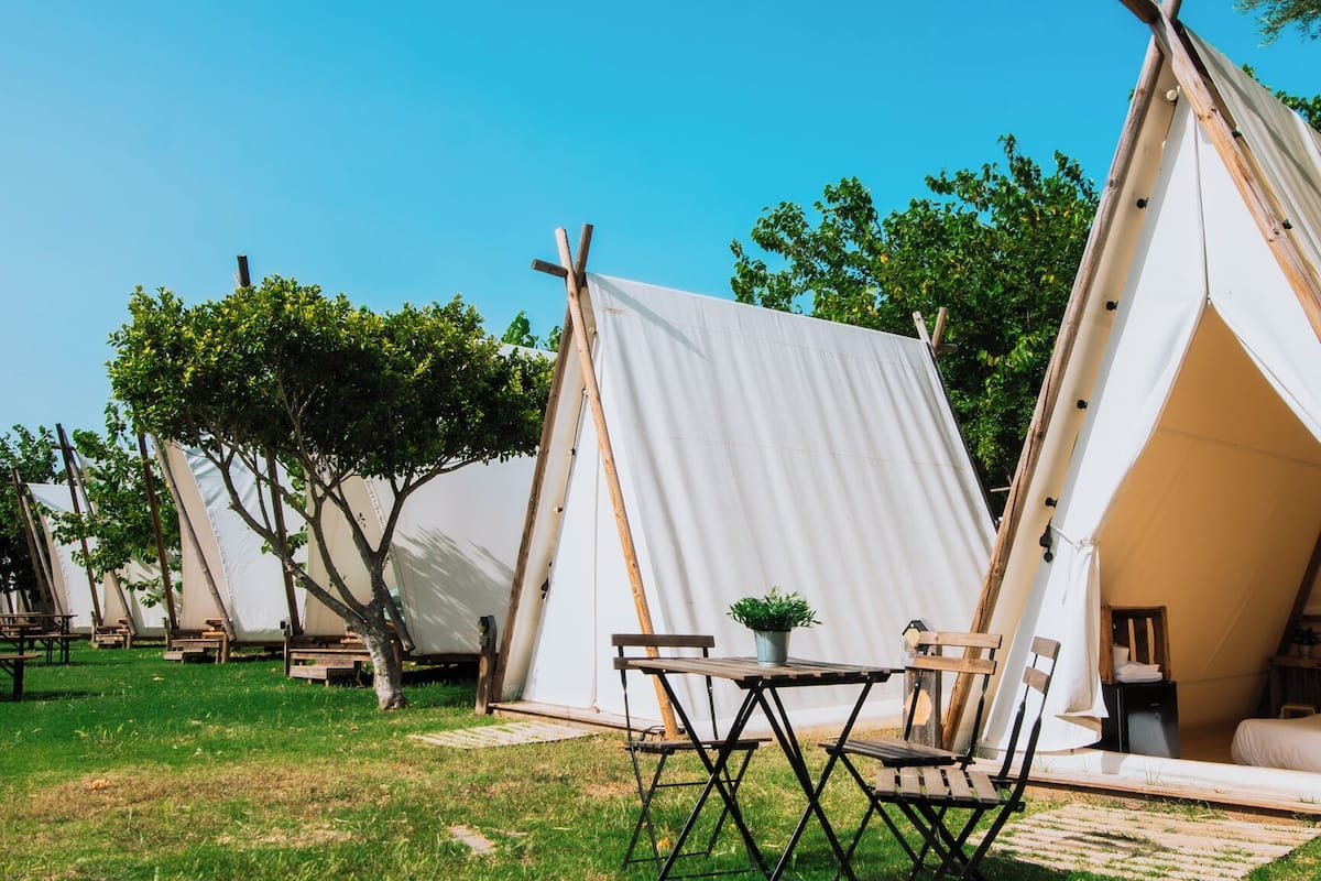 A series of A-frame tents with picnic tables and chairs in a grassy area.