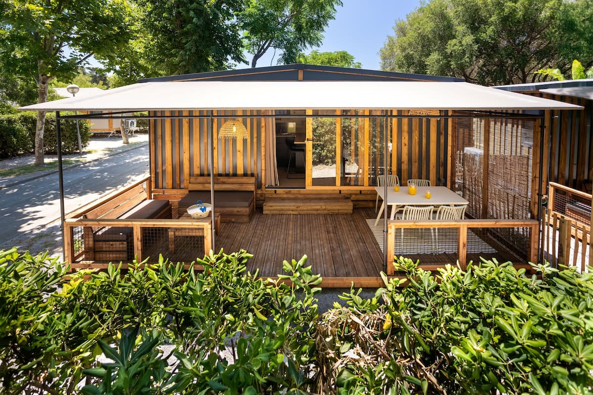 A wooden outdoor patio with a table and chairs, a bench, and a covered seating area.