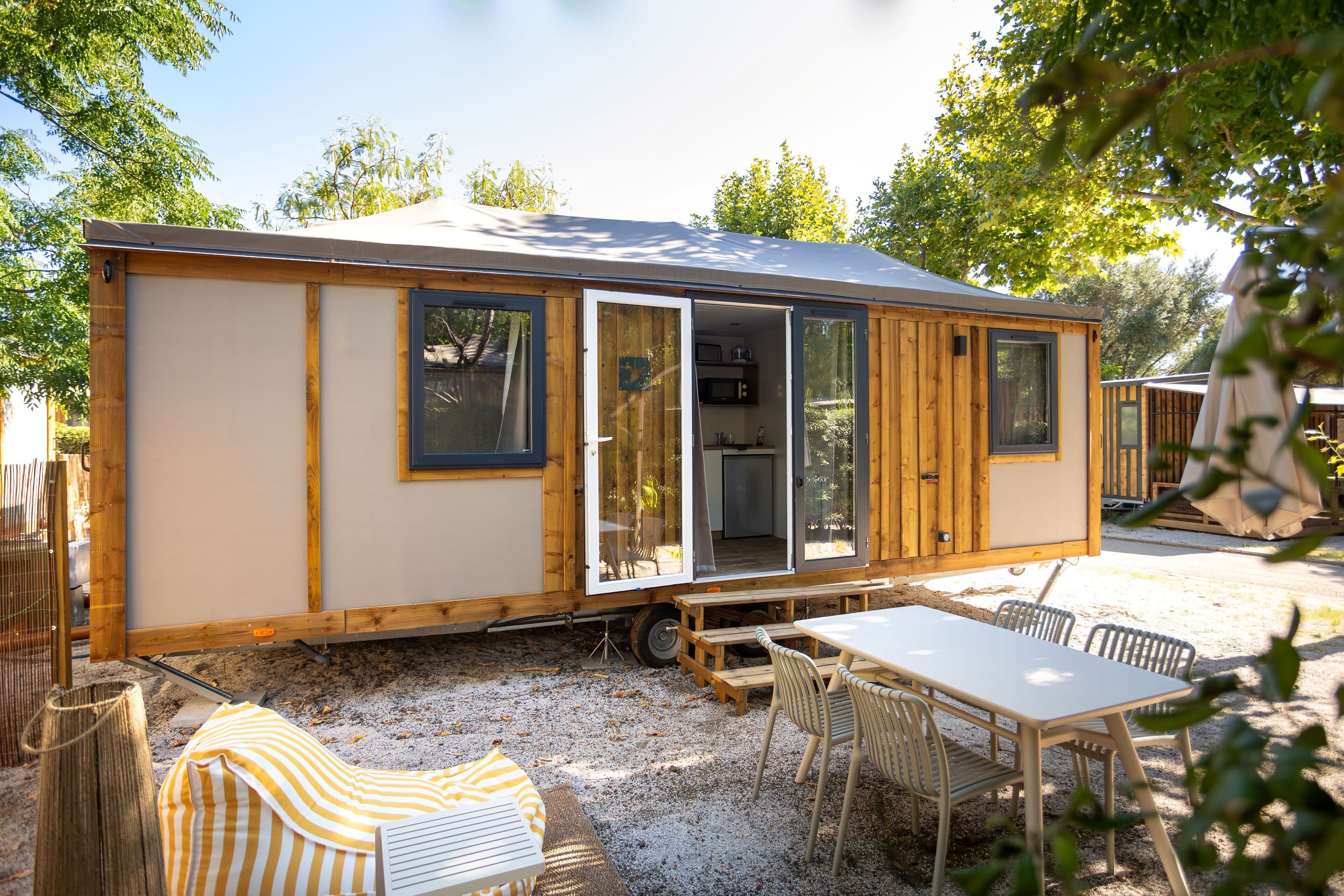 Una casa móvil con puerta corredera, un pequeño patio con mesa y sillas, y un espacio exterior cubierto.