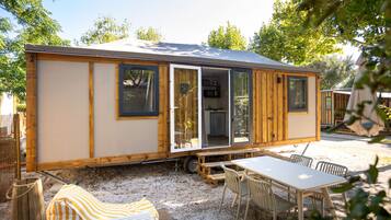 Una casa móvil con puerta corredera, un pequeño patio con mesa y sillas, y un espacio exterior cubierto.