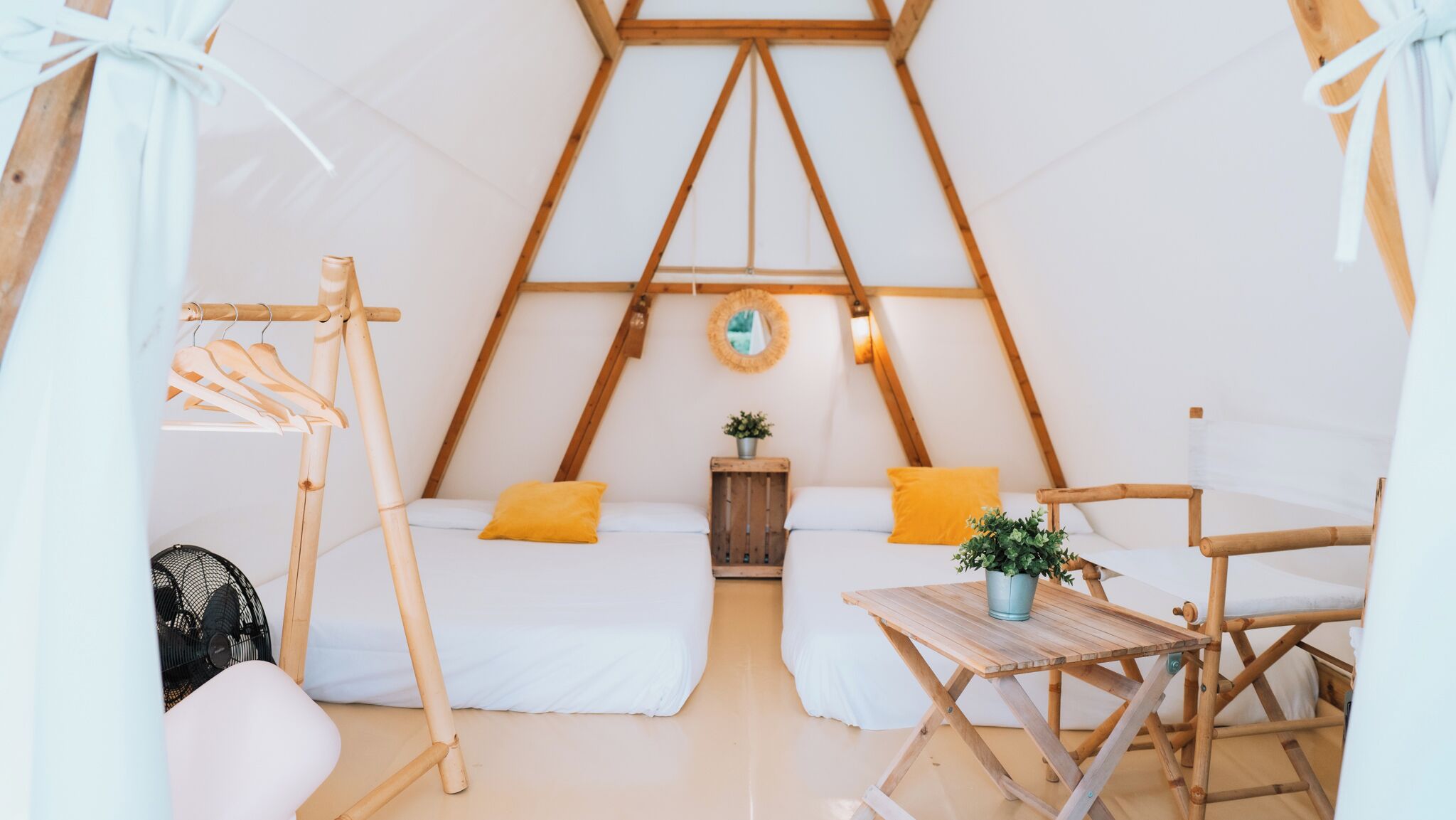 Una habitación tipo tienda de campaña, acogedora y triangular, con dos camas, una mesita y un ventilador.