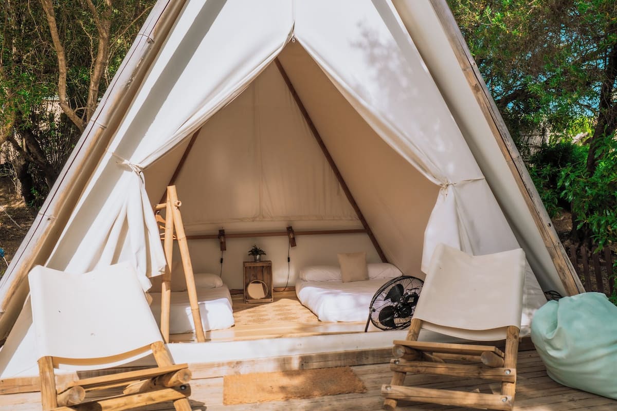 A tent with a bed, two chairs, and a fan.