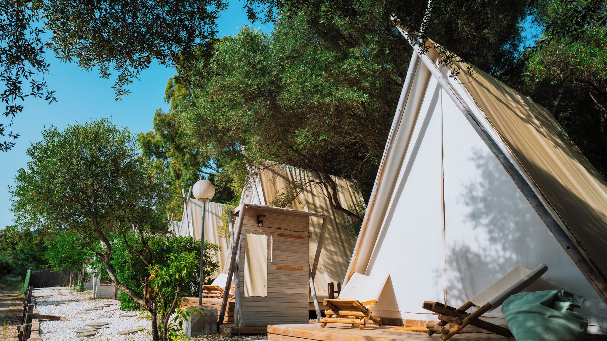 Un terrain de camping avec plusieurs tentes, une terrasse en bois et un lampadaire.