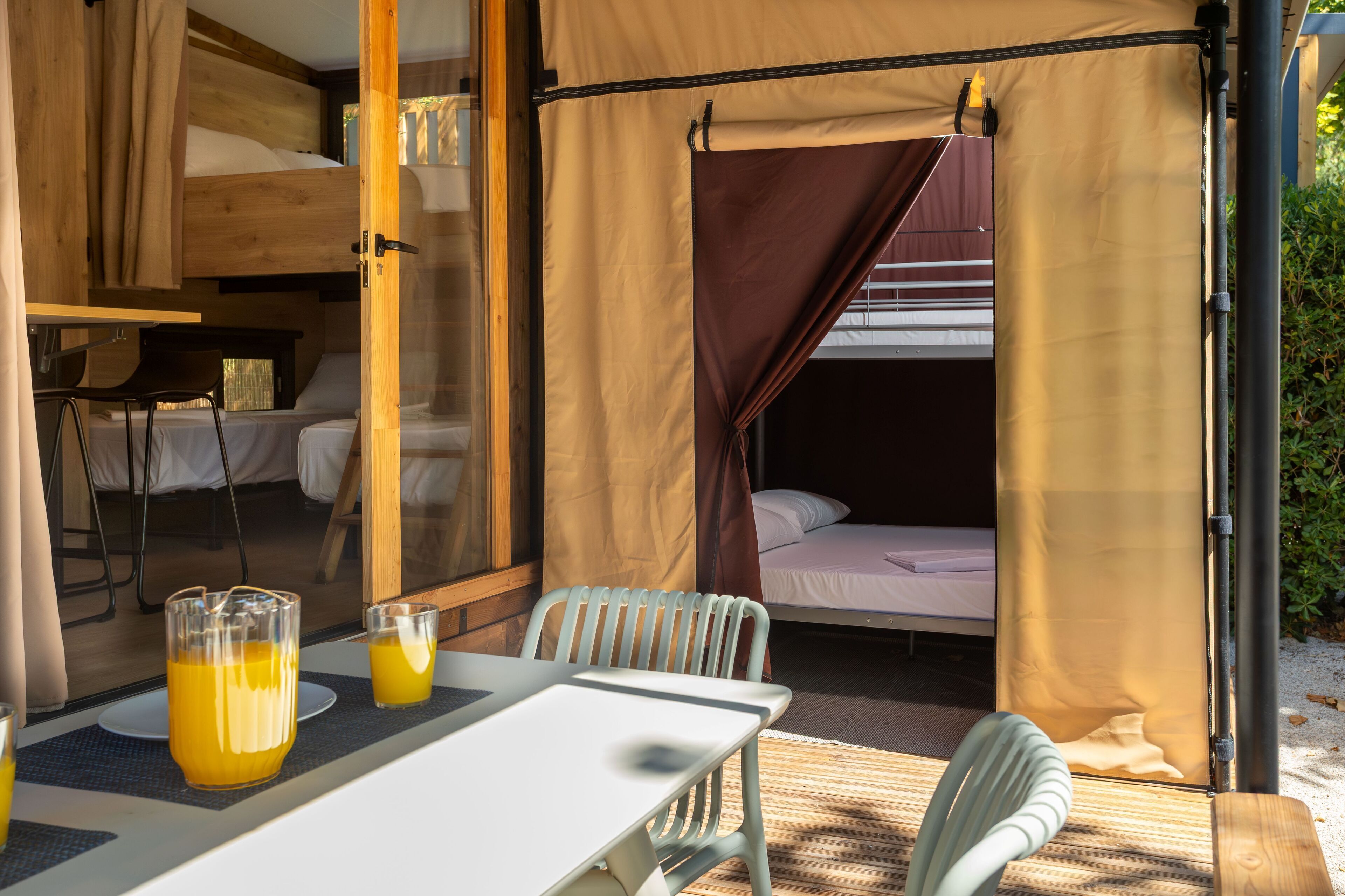 Una habitación acogedora y bien iluminada con una litera, una mesa con una silla y un vaso de jugo de naranja.