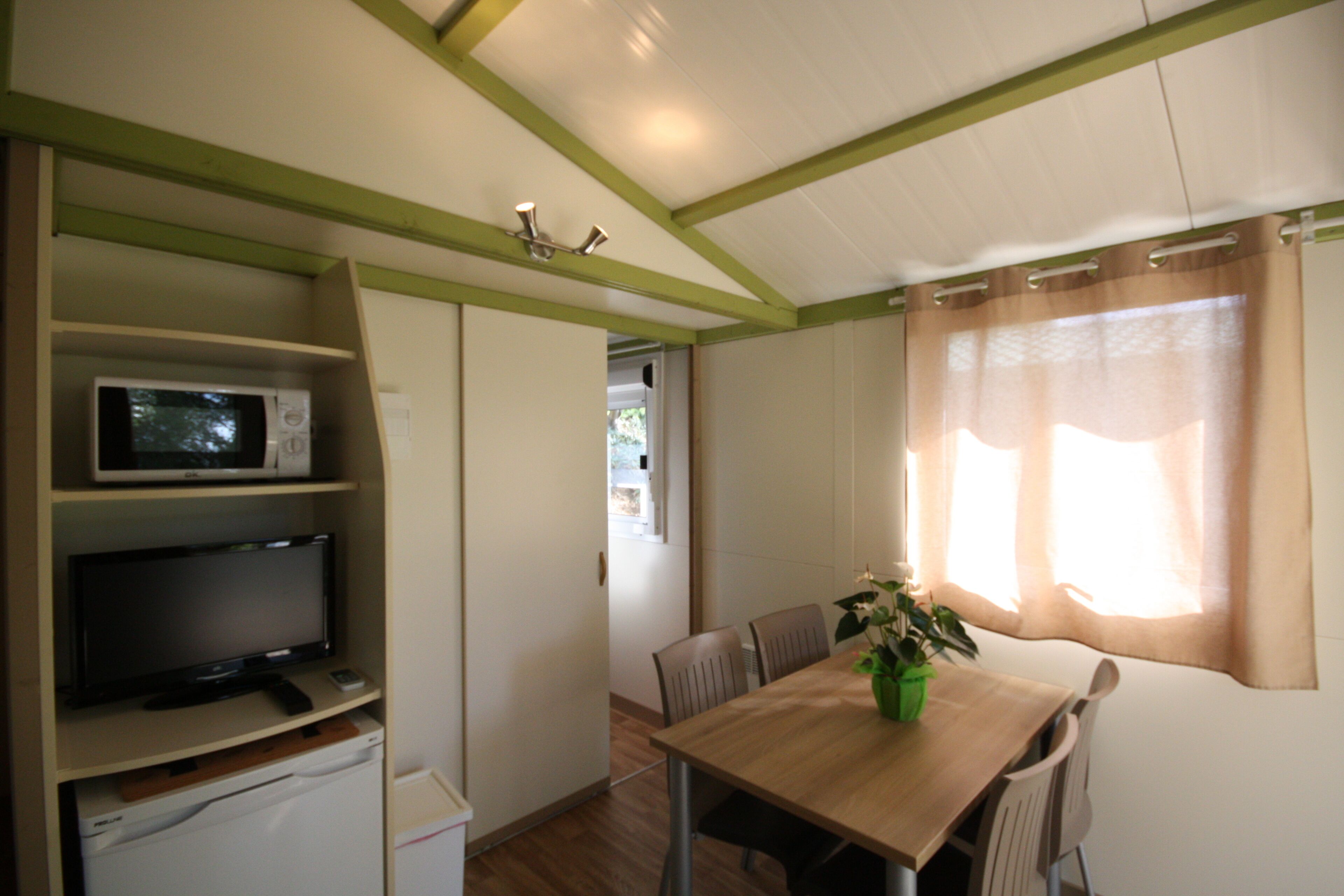 Een kleine kamer met een eettafel, stoelen, een magnetron en een televisie op een plank.
