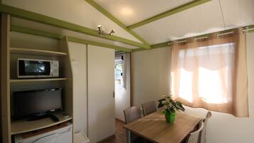 Een kleine kamer met een eettafel, stoelen, een magnetron en een televisie op een plank.