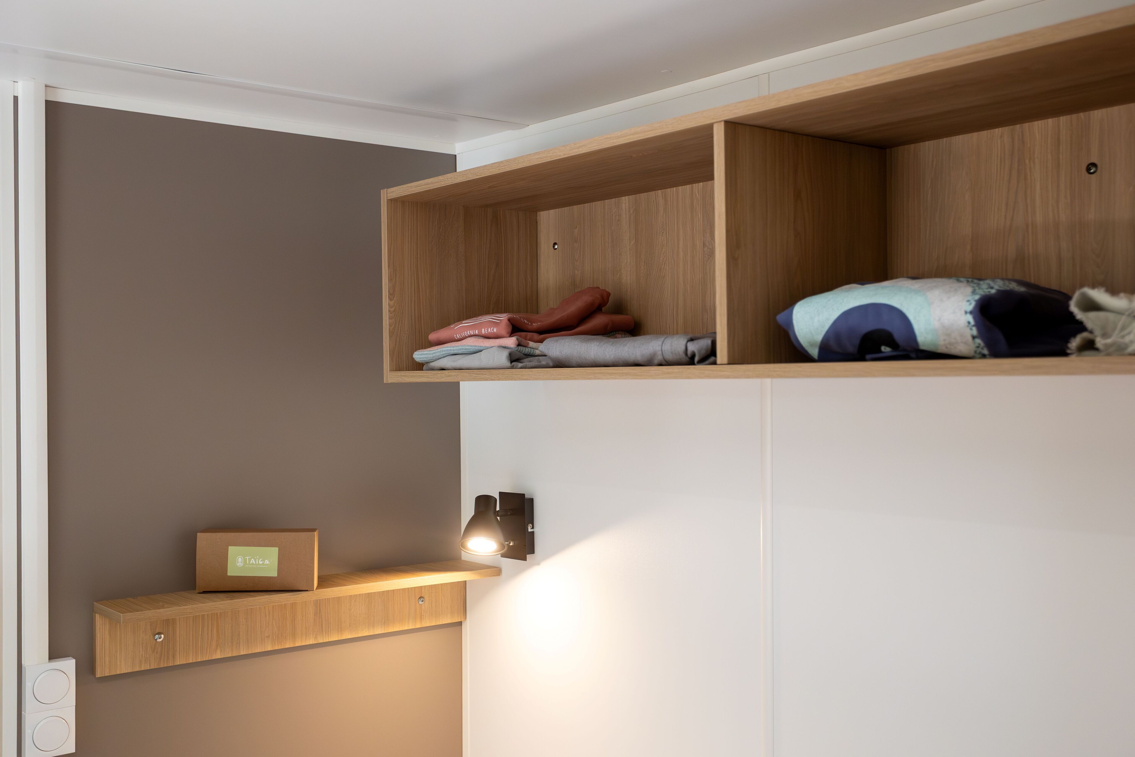 A room with a wooden shelf unit containing folded clothes and a box labeled "Taiga."