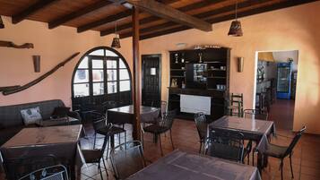 Un restaurante con vigas de madera, un gran ventanal arqueado y una estantería negra. Mesas y sillas dispuestas para comer.
