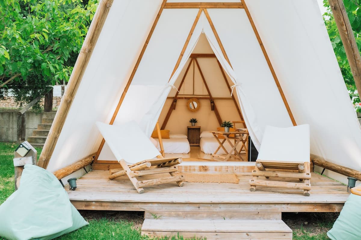 A cozy, triangular tent with a wooden floor, two beds, a small table, and a chair.