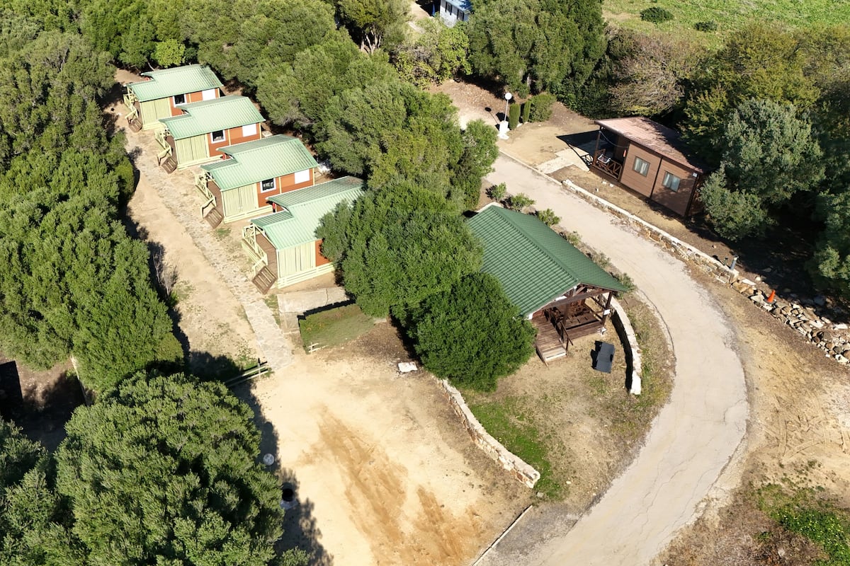 An aerial view of a campsite with several cabins, a central communal area, and surrounding dense forest.