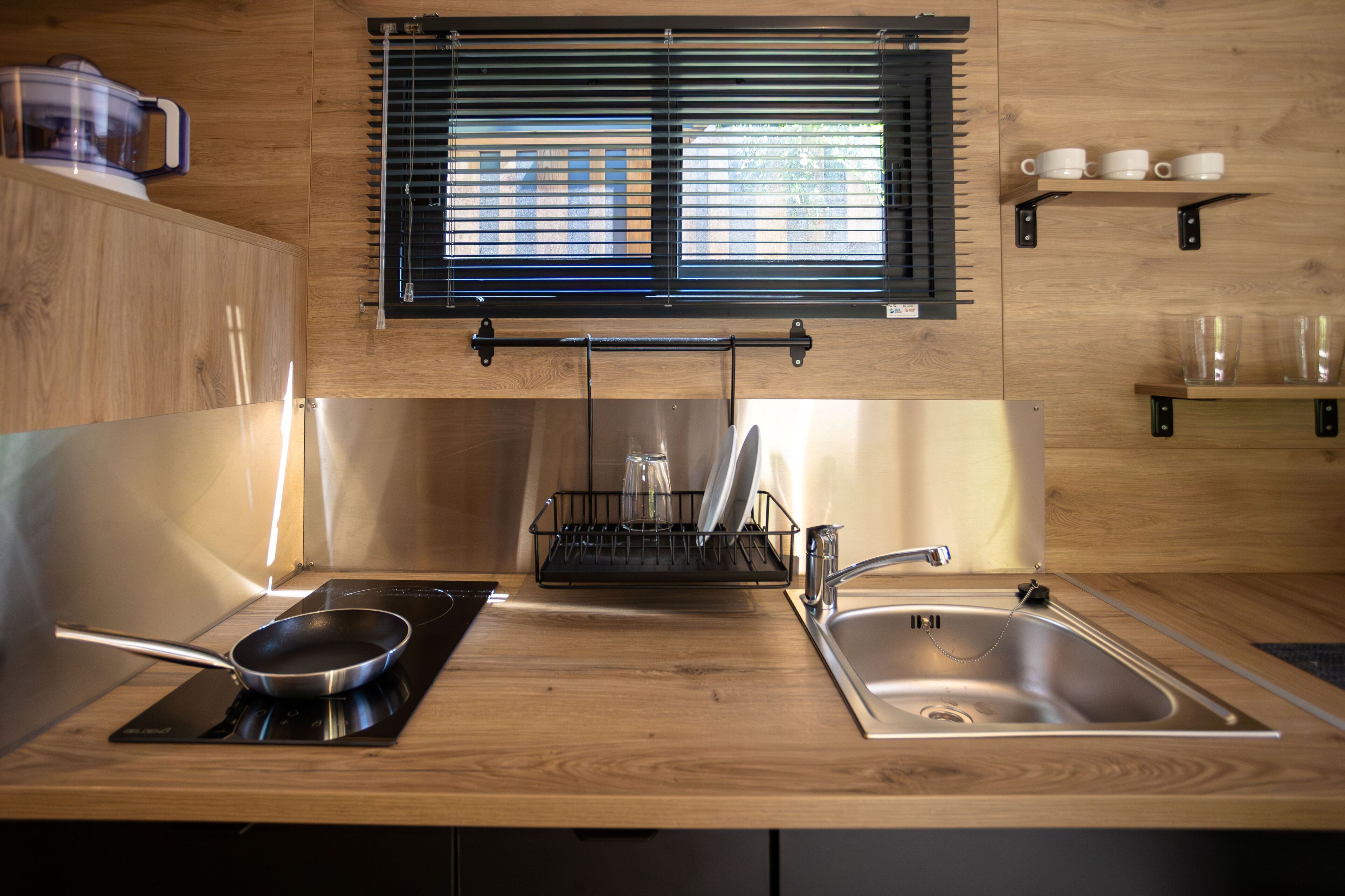 A modern kitchen with a wooden countertop, a built-in stove, a sink, and a window with blinds.