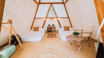 Une pièce confortable, aménagée comme une tente triangulaire, avec deux lits, une petite table et une chaise.