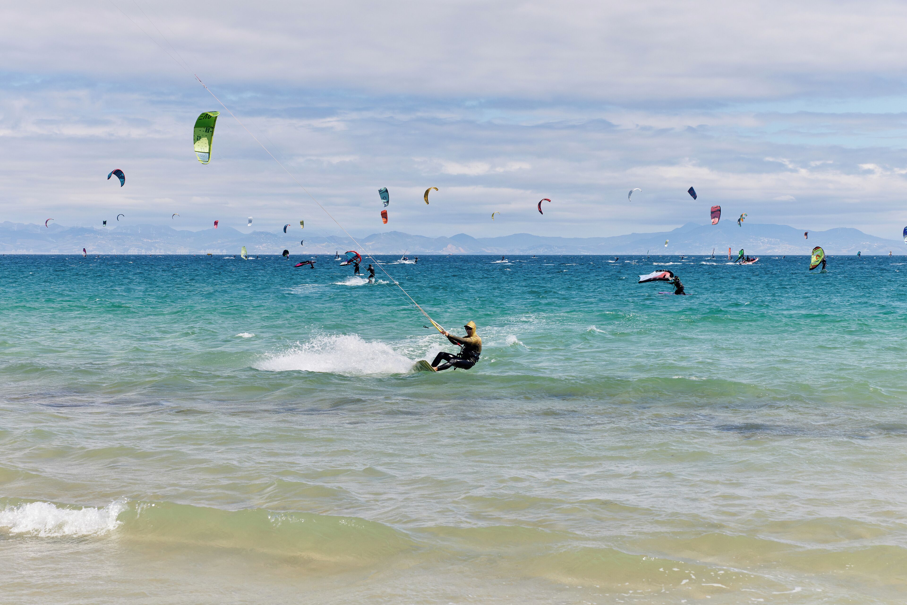A beach with people windsurfing and parasailing.