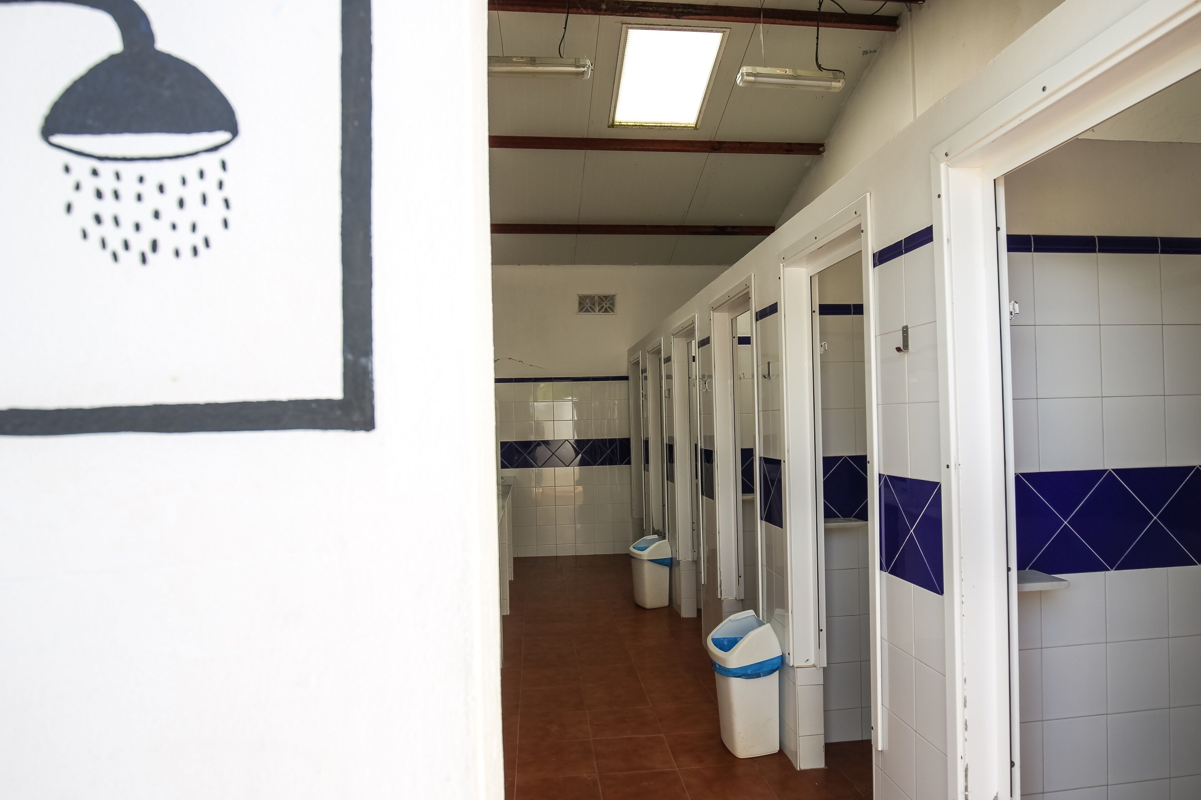 A hallway with multiple stalls, each with a white tiled wall and a blue accent.