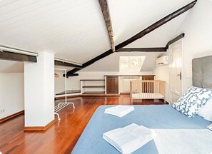 Ein Schlafzimmer mit schrägen Wänden, einem Kinderbett, einem Bett mit blauer Matratze und einem weißen Heizkörper.