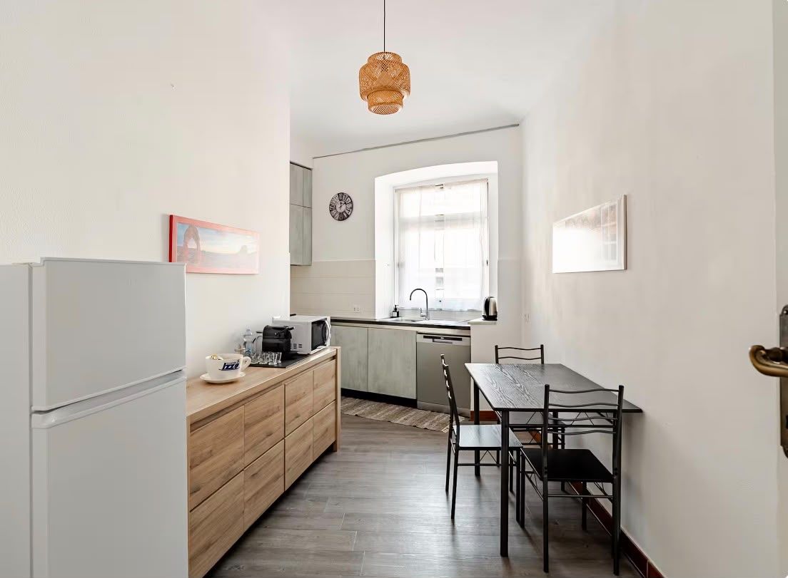 A compact kitchen with a refrigerator, wooden cabinets, a coffee maker, and a dining table with chairs.