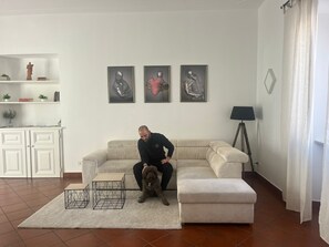 Een woonkamer met een bank, een klein tafeltje, een hond en drie ingelijste kunstwerken aan de muur.
