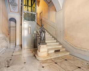 A marble staircase with a statue, a glass elevator, and a metal gate.