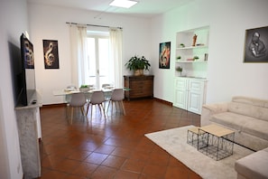 Un salon avec un canapé, un coin repas avec des chaises, un téléviseur, une plante et des œuvres d’art accrochées aux murs.