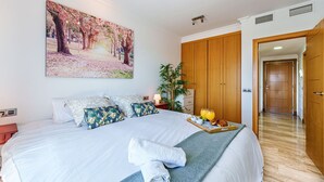 A hotel room with a large bed, a painting of a park, a wooden wardrobe, and a tray with breakfast items.