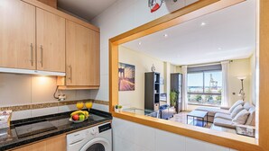 A modern kitchen with wooden cabinets, a washing machine, and a dining area with a sofa and table.