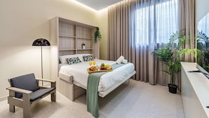 Un dormitorio moderno con cama, mesita de noche, silla y un amplio ventanal con cortinas.