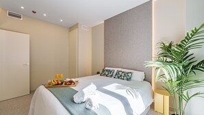 A hotel room with a bed, a tray with fruits and drinks, a potted plant, and a bedside table. - Sunset Malaga Apartments - WIDE 1+2+3 (Málaga)