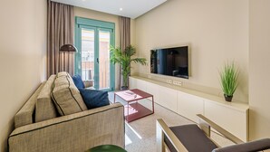 A modern living room with a sofa, a coffee table, a TV mounted on the wall, and a balcony with curtains. - Sunset Malaga Apartments - WIDE 1+2+3 (Málaga)