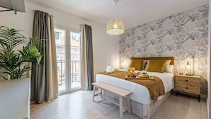 A bedroom with a bed, bedside table, bench, and a view of the outside.