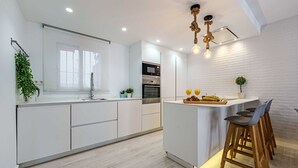 A modern kitchen with white cabinetry, a central island with bar stools, a built-in oven, and a hanging light fixture.