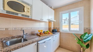 Una cocina con encimera de granito, un fregadero, lavavajillas y ventana con vista a edificios.