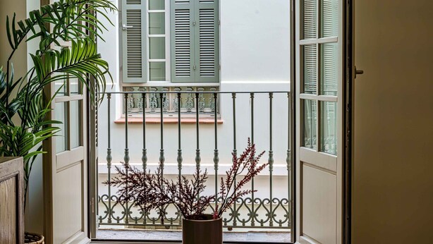 A balcony with a wrought iron railing, a potted plant, and a view of a building with green shutters.