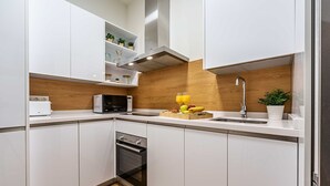 A modern kitchen with white cabinets, a microwave, a toaster, a sink, and a wooden backsplash.