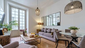 A modern living room with a sofa, chairs, a dining table, and a large window.