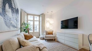 Ein modernes Wohnzimmer mit einem beigefarbenen Sofa, einem weißen Schrank, einem Flachbildfernseher und einem großen abstrakten Gemälde.
