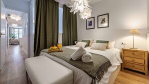 Ein modernes Schlafzimmer mit einem großen Bett, einem Nachttisch, einer Lampe und Blick auf einen Flur.