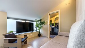 A modern living room with a sofa, a TV, a potted plant, and a small table.