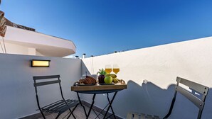 A balcony with a table set for a meal, including fruits and glasses, and a bench.