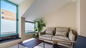 Un salon moderne avec un canapé, une table basse et une grande fenêtre donnant sur un immeuble.