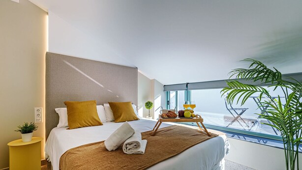 Une chambre d’hôtel moderne avec un grand lit, un chariot de service pour le petit-déjeuner, une plante en pot et une vue sur la mer.