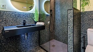Une salle de bain moderne avec un lavabo en granit noir, une douche en verre et un miroir doté d’un éclairage circulaire.