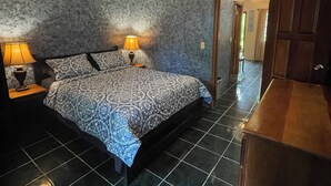 Quarto com uma cama, duas mesas de cabeceira com luminárias, um aparador de madeira e uma porta para outro cômodo.
