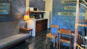 Uma sala de estar aconchegante com sofá, cadeiras, luminária, cozinha com micro-ondas, geladeira e cafeteira.