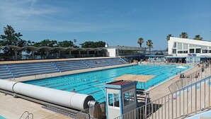 A large outdoor swimming pool with multiple lanes, a lifeguard tower, and a beach area.